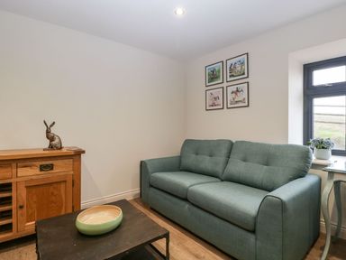A sitting room with a green sofa a wooden cabinet a black coffee table and framed pictures on the wall at Palace Farmhouse in St Weonards