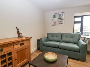 A living room with a green sofa a wooden cabinet with a sculpture and framed pictures on the wall at Palace Farmhouse in St Weonards