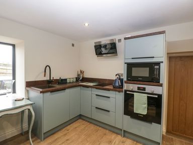 A kitchen with blue cabinets a black sink and faucet a microwave oven a kettle and a wooden floor at Palace Farmhouse in St Weonards