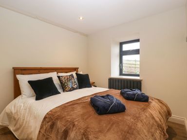 A bedroom with a wooden bed frame white bedding brown blanket two navy blue robes on bed and a small window at Palace Farmhouse in St Weonards