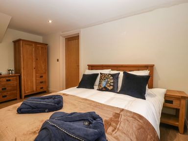 A bedroom with a wooden bed frame white bedding and dark blue pillows with a wardrobe and chest of drawers at Palace Farmhouse in St Weonards