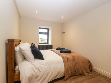 A bedroom with a wooden bed frame white bedding brown blanket blue pillows and a window at Palace Farmhouse in St Weonards