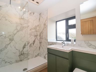 A bathroom with a marble shower enclosure a green vanity unit a white sink and a window at Palace Farmhouse in St Weonards