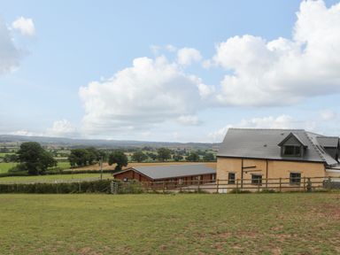 A rural landscape with a yellow building and wooden structure surrounded by fields at Palace Farmhouse in St Weonards