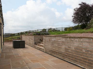 An outdoor patio with stone flooring a small black table low brick walls and steps leading to a grassy area with flowers and a tree at Palace Farmhouse in St Weonards