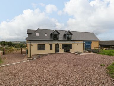 A modern house with a sloped roof and multiple windows with a gravel driveway at Palace Farmhouse in St Weonards