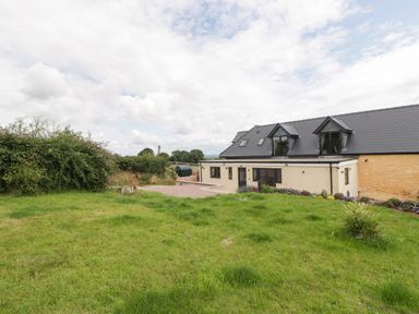 A grassy yard with bushes and a gravel path next to a building with dormer windows at Palace Farmhouse in St Weonards