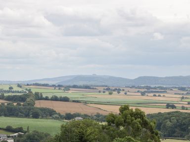 A rural landscape with fields trees and hills under a cloudy sky at Palace Farmhouse in St Weonards