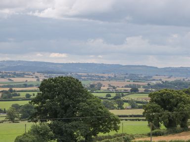 A rural landscape with fields trees and hills under a cloudy sky at Palace Farmhouse in St Weonards