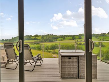 A balcony with chairs and a table overlooking green hills at Bwncath Garthmyl