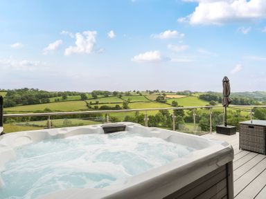 A hot tub with outdoor furniture and a landscape view at Bwncath in Garthmyl