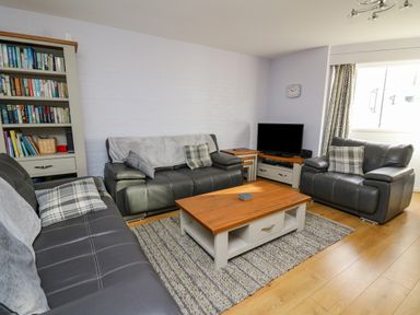 A living room with three leather sofas a wooden coffee table a bookshelf and a television at 1 St Marys Court in Tenby