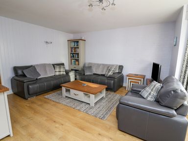 A living room with grey leather sofas a wooden coffee table a rug a bookcase and a television at 1 St Marys Court Tenby