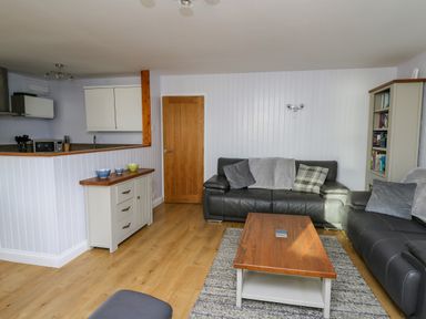A living room with black leather sofas wooden coffee table and a kitchen area at 1 St Marys Court in Tenby