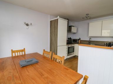 A kitchen and dining area with a wooden table and chairs and white cabinets at 1 St Marys Court in Tenby