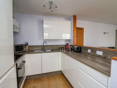A kitchen with white cabinets a microwave oven a sink toaster kettle and wooden floor at 1 St Marys Court in Tenby