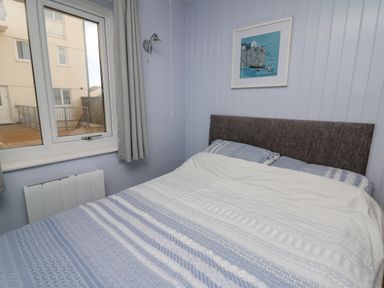 A bedroom with a bed with patterned bedding a window and a framed picture on the wall at 1 St Marys Court in Tenby