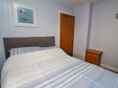 A bedroom with a bed blue and white bedding wooden door wooden nightstand and a framed picture on the wall at 1 St Marys Court in Tenby