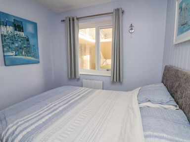 A bedroom with a bed covered in blue and white bedding a window with gray curtains and artwork on the walls at 1 St Marys Court in Tenby
