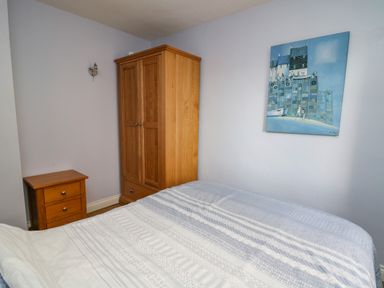 A bedroom with a bed covered by a patterned duvet a wooden wardrobe a wooden bedside table and a painting on the wall at 1 St Marys Court in Tenby