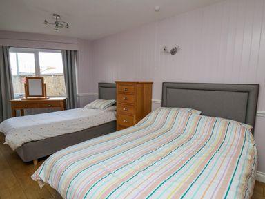 A bedroom with two beds a wooden chest of drawers and a dressing table by the window at 1 St Marys Court in Tenby
