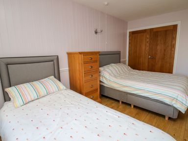 A bedroom with two single beds joined together with striped bedding a wooden chest of drawers and double wooden doors at 1 St Marys Court in Tenby