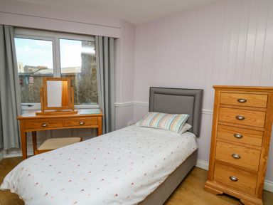 A bedroom with a single bed a wooden dressing table and a wooden chest of drawers at 1 St Marys Court in Tenby