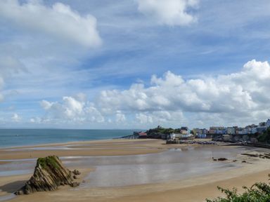 A beach with rocks and a pier near a town with colorful buildings at 1 St Marys Court in Tenby