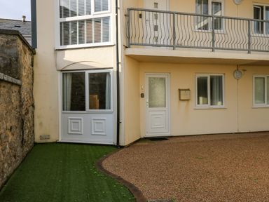 An exterior view of a beige building with a white door and windows above and beside a gravel path at 1 St Marys Court in Tenby