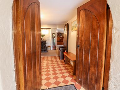 View through wooden double doors into hallway with checkerboard floor bench painting and grandfather clock at Twelve Oaks Farmhouse in Teigngrace near Newton Abbot