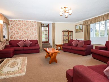 A living room with red sofas a wooden coffee table a glass display cabinet and floral wallpaper at Twelve Oaks Farmhouse Teigngrace near Newton Abbot