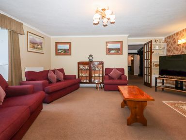 A living room with red sofas a wooden coffee table a display cabinet and a television at Twelve Oaks Farmhouse in Teigngrace near Newton Abbot