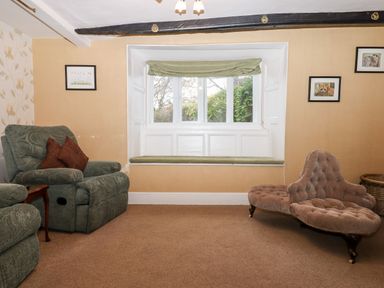 A sitting room with a window seat green armchairs and a tufted brown loveseat at Twelve Oaks Farmhouse Teigngrace near Newton Abbot