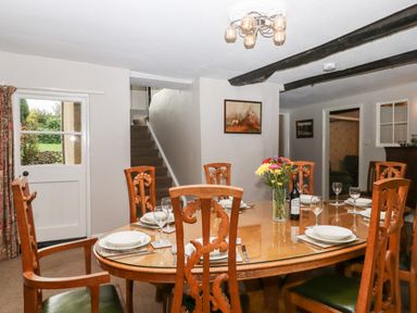 A dining room with a wooden table and chairs set with plates glasses and a vase of flowers at Twelve Oaks Farmhouse in Teigngrace near Newton Abbot