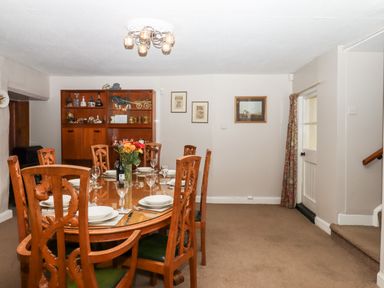 A dining room with a wooden table set for six and a cabinet with decorations at Twelve Oaks Farmhouse in Teigngrace near Newton Abbot