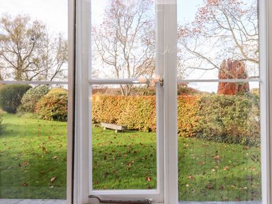A garden view with green grass fallen leaves bushes and trees seen through a window at Twelve Oaks Farmhouse Teigngrace near Newton Abbot