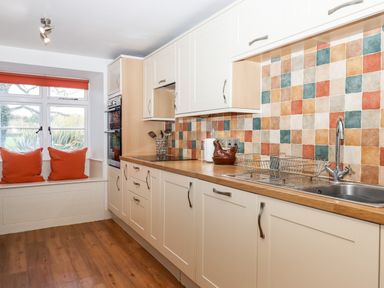 A kitchen with wooden countertops colorful tiled backsplash a stainless steel sink and a window seat with orange cushions at Twelve Oaks Farmhouse Teigngrace near Newton Abbot