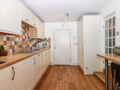 A kitchen with white cabinets wooden countertops multicolored tiled backsplash a metal sink and faucet and a wooden floor at Twelve Oaks Farmhouse Teigngrace near Newton Abbot