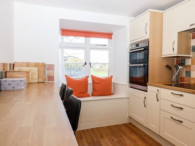 A kitchen with wooden countertops black chairs a window seat with orange cushions and built in ovens at Twelve Oaks Farmhouse in Teigngrace near Newton Abbot