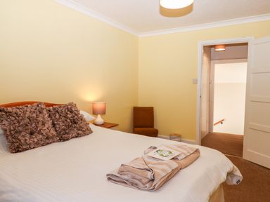 A bedroom with a bed with textured pillows a bedside table lamp a chair and an open door showing a hallway at Twelve Oaks Farmhouse in Teigngrace near Newton Abbot