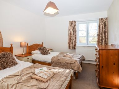 A bedroom with two single beds a wooden dresser and window with curtains at Twelve Oaks Farmhouse in Teigngrace near Newton Abbot