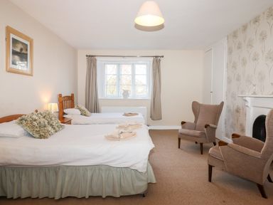 A bedroom with two single beds a window with curtains two armchairs and a fireplace at Twelve Oaks Farmhouse in Teigngrace near Newton Abbot
