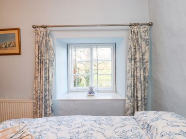 A bedroom window with patterned curtains and a bed with a patterned bedspread at Twelve Oaks Farmhouse Teigngrace near Newton Abbot