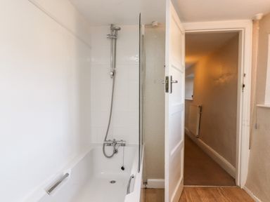 A bathroom with a bathtub and showerhead next to an open door showing a hallway at Twelve Oaks Farmhouse Teigngrace near Newton Abbot