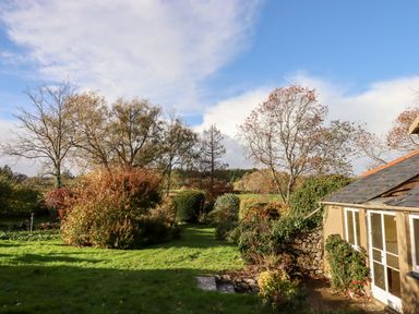 A garden with grass, bushes, and trees next to a house with glass doors at Twelve Oaks Farmhouse in Teigngrace near Newton Abbot