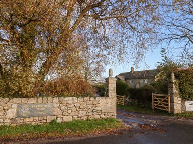 A stone wall with a sign reading Twelve Oaks Herd and a gated entrance to a property with a house and trees at Twelve Oaks Farmhouse in Teigngrace near Newton Abbot