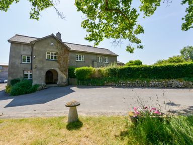 A two-story building with an arched entrance surrounded by greenery and a driveway at Twelve Oaks Farmhouse in Teigngrace near Newton Abbot