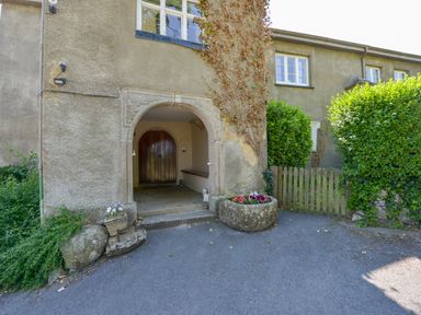 Arched stone entrance with wooden door and flower pots in front of a stone building with windows and ivy at Twelve Oaks Farmhouse in Teigngrace near Newton Abbot