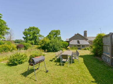 A garden with a barbecue grill and a large table with chairs in front of a house at Twelve Oaks Farmhouse Teigngrace near Newton Abbot