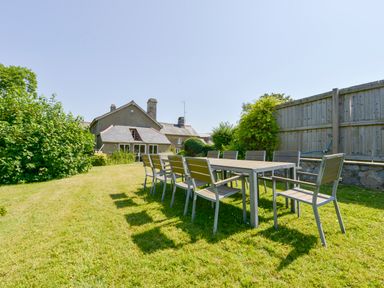An outdoor dining table with eight chairs on grass in a garden with a house and wooden fence in the background at Twelve Oaks Farmhouse in Teigngrace near Newton Abbot